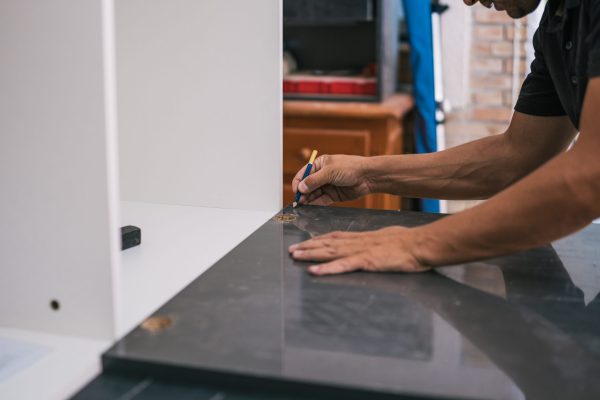 Detail of a man's hands drawing a line on a surface with a pencil in a workshop.